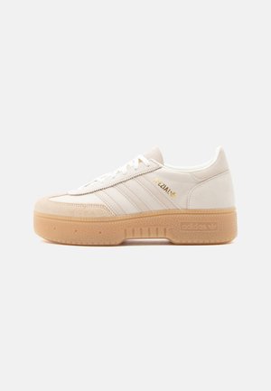 Adidas Spezial off-white leather sneaker with gum rubber platform sole, white stripes, gold logo, and suede toe cap, side view on white background.