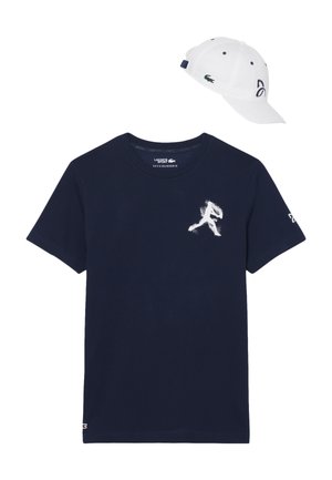 Maglietta a maniche corte blu navy con grafica bianca di un giocatore di baseball e cappello bianco con logo verde e cinturino regolabile blu scuro.
