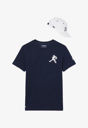 Maglietta a maniche corte blu navy con grafica bianca di un giocatore di baseball e cappello bianco con logo verde e cinturino regolabile blu scuro.