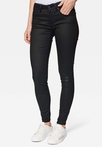 Schwarze, schlank geschnittene Jeans mit Taschen, aus elastischem Material. Kombiniert mit weißen Sneakers mit einem strukturierten Akzentpanel.