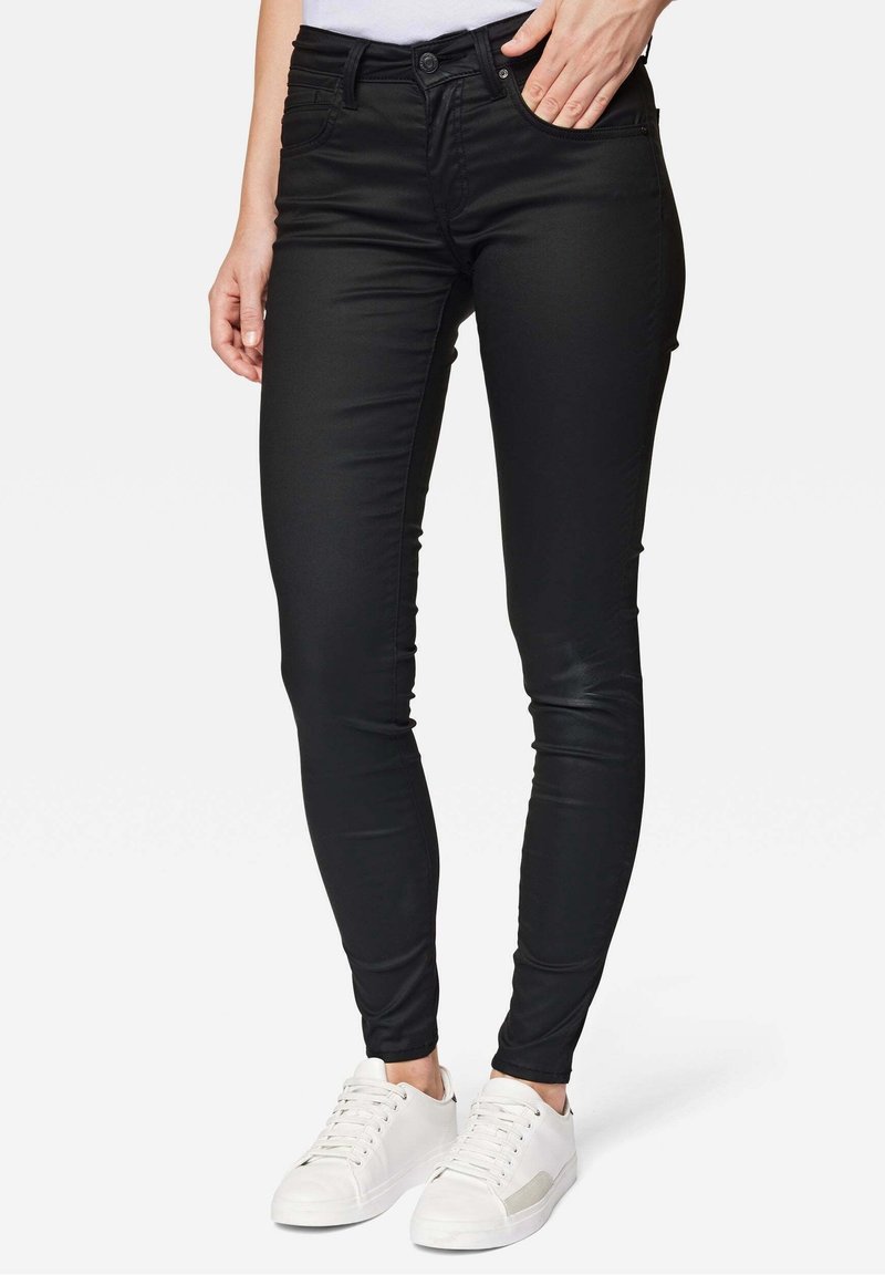 Schwarze, schlank geschnittene Jeans mit Taschen, aus elastischem Material. Kombiniert mit weißen Sneakers mit einem strukturierten Akzentpanel.