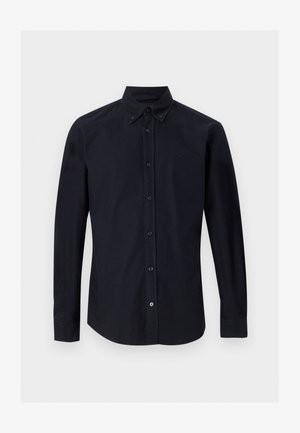 Chemise noire à manches longues boutonnée, col pointu et logo brodé discret sur la poitrine gauche, présentée sur un fond uni.