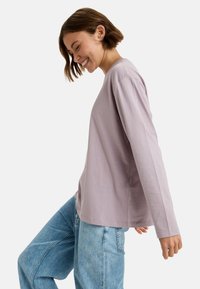 Långärmad lavendelfärgad t-shirt i mjuk bomull, med avslappnad passform och rund halsringning, ihop med ljusblå jeans.