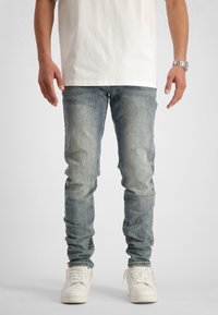 Ljusblå skinny jeans med subtila blekningar, tillverkade av denim, i kombination med vita högtoppsneakers och en enkel vit t-shirt.