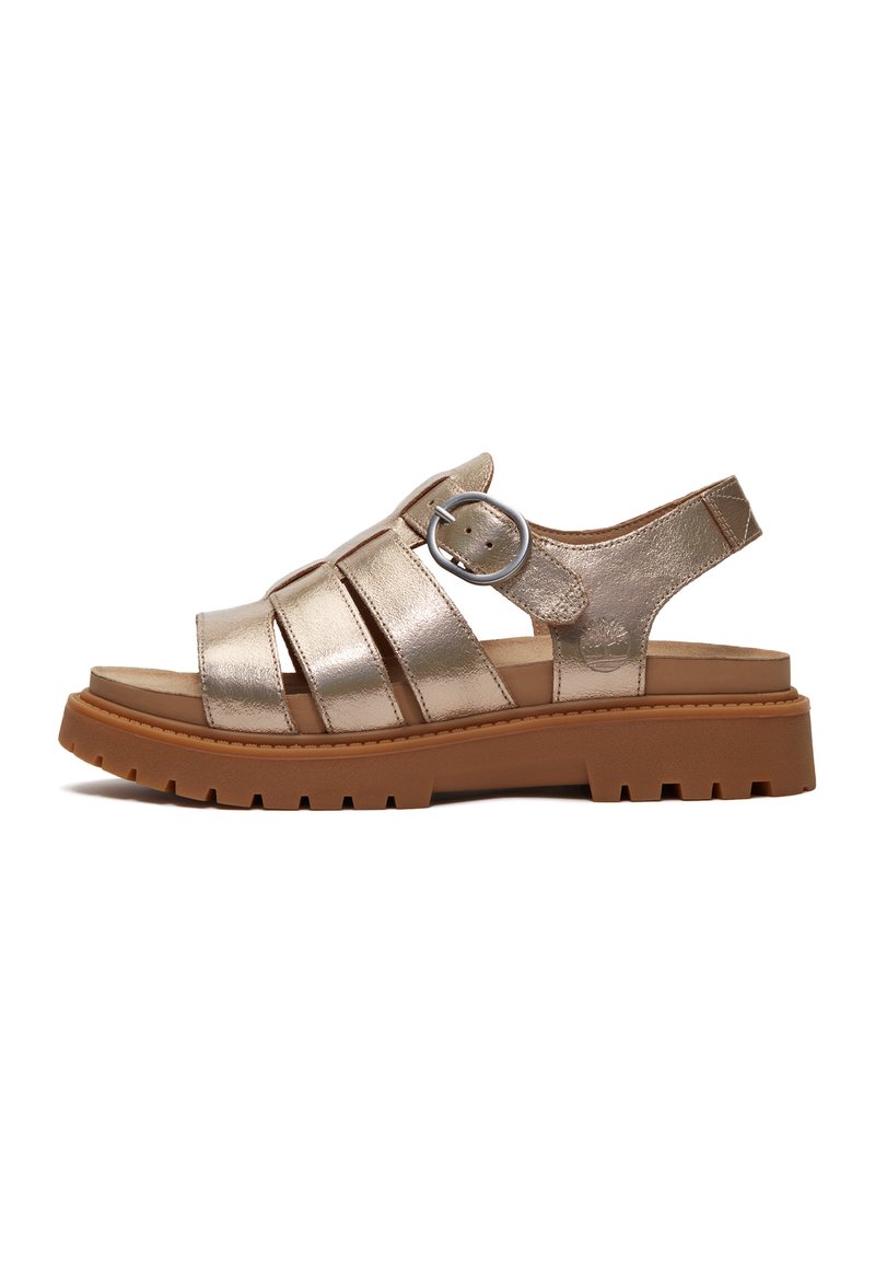 Metallic gold sandal with three crossover straps, a round silver buckle, and a chunky brown textured sole. Open back design for easy wear.
