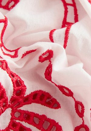 White fabric with intricate red embroidery, featuring loops and swirls. The texture is soft with a lightweight, airy appearance.