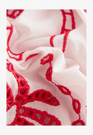 White fabric with intricate red embroidery, featuring loops and swirls. The texture is soft with a lightweight, airy appearance.