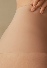 Naadloze huidskleurige panty met een zachte, gladde textuur, voorzien van een dunne, rekbare band aan de bovenkant voor een veilige pasvorm zonder zichtbare lijnen.