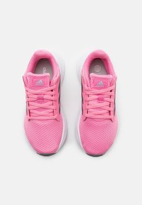 Różowe buty sportowe z siateczkową cholewką i syntetycznymi akcentami, z sznurowanym zapięciem i wyściełaną podeszwą. Czarny detal wzdłuż boków.