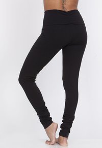 Svarta leggings gjorda av stretchigt tyg, med hög midja och rynkade detaljer, som smalnar av för att forma bena. Mjuk textur, ankellängd.