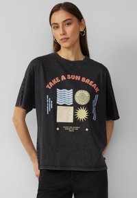 Schwarzes übergroßes T-Shirt aus weichem Baumwoll-Mix mit Grafik auf der Vorderseite. Mit buntem Text, Wellen, Sonnenmotiven und einem Retro-Design.
