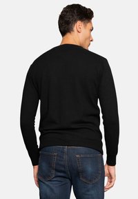 Black sweater with a round neckline and long sleeves, made from a soft, textured fabric. Worn with blue jeans featuring rear pockets.