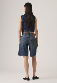 Veste en jean au design court avec des accents de boutons, associée à un short en jean à coupe décontractée et poches arrière. Couleur bleu marine.