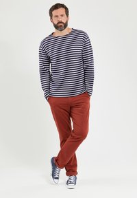 Marineblå og hvide stribede langærmede skjorte, parret med rustfarvede bukser og marineblå sneakers. Outfitet har en afslappet pasform og er lavet af bomuldsstof.