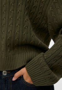 Oliwkowy sweter z dzianiny, ozdobiony teksturowym wzorem w warkocze i ściągaczami, o luźnym kroju i widocznymi detalami szwów.