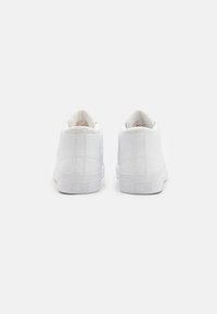 Zapatillas altas blancas con un acabado de cuero suave, punta redonda, forro interior en contraste, y "Converse All Star" grabado en el talón.