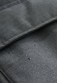 Nahaufnahme von schwarzem wasserdichtem Stoff mit sichtbaren Wassertröpfchen auf der Oberfläche und gefalteten Nähten.