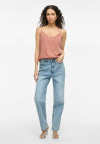 Camisola din satin roz pal cu bretele subțiri, asociată cu blugi cu talie înaltă de un albastru deschis. Modelul poartă de asemenea sandale cu toc înalte alb-negru.