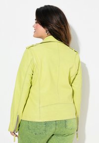 Veste en cuir vert lime avec épaulettes et poignets zippés, présentant un design ajusté et une texture lisse. Vue arrière montrée.