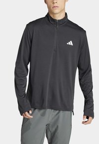 Schwarzes, langärmliges Sportoberteil mit Viertelreißverschluss, aus glattem Stoff gefertigt, mit einem weißen Logo auf der Brust und einer lockeren Passform.