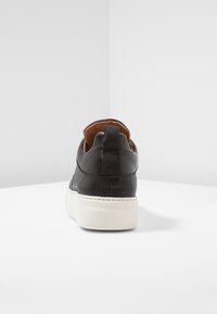 Svart läder sneaker med hög bakdel, kontrasterande brun innersula och en vit gummisula. Har en texturerad hälpulltab.