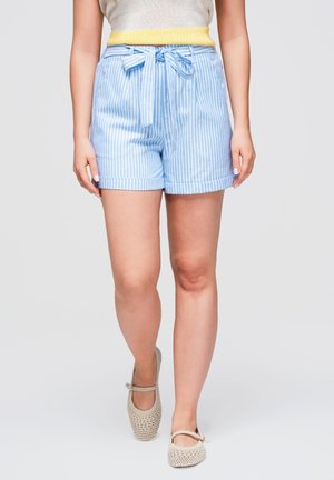 Personne portant un short rayé bleu clair et blanc avec une ceinture nouée, des chaussures Mary Jane en tricot couleur crème et un débardeur avec un ourlet jaune.
