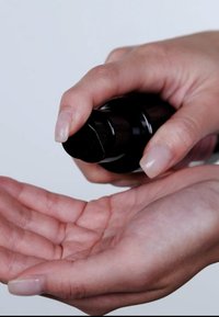 Czarna pompka butelki jest naciskana, wydobywając produkt na otwartą dłoń. Gładka tekstura skóry z naturalnym paznokciem. Minimalistyczne tło.