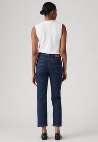 Tumed sinised denim püksid sirge säärega, keskmise kõrgusega talje ja kahe tagataskuga, millel on logoplaat ja õmbluse detail.