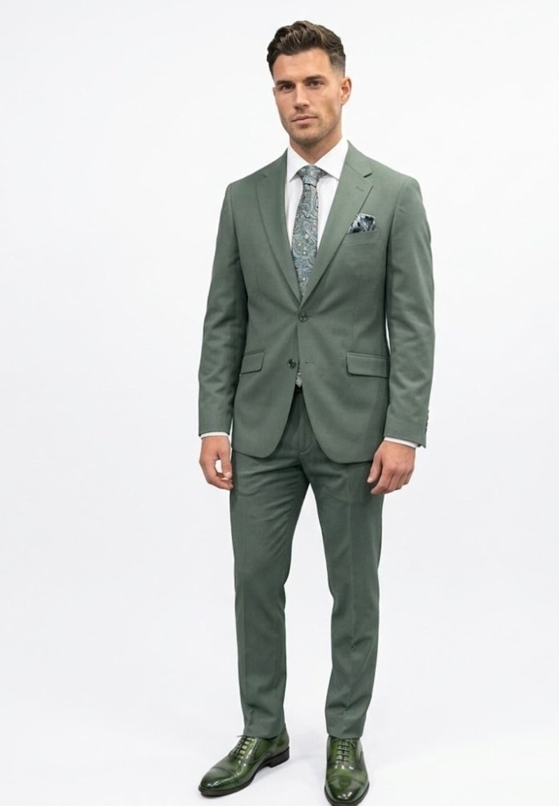 Hombre vestido con un traje verde ajustado, corbata y pañuelo de bolsillo a juego con patrón, camisa blanca y zapatos de vestir verdes pulidos, posando frente a un fondo blanco.