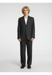 Svart dress med enblads knappeblazer, bukser med flatt frontparti og ensfarget hvit t-skjorte under. Glatt stoff med skreddersydd passform.