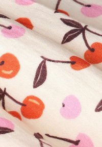 Tissu en coton avec un motif répétitif de cerises orange et roses avec des tiges et des feuilles marron foncé sur un fond crème.