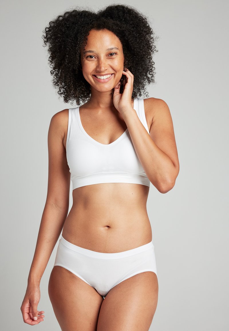WeißesStretchstoff-Bralette mit V-Ausschnitt und breiten Trägern, kombiniert mit passenden hochgeschnittenen Slip. Glatte Textur mit körpernahem Design.