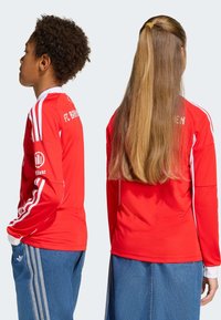 Rode lange mouwen trui met witte accenten. Voorzien van het FC Bayern-logo, ronde hals en gestreepte mouwen. Gecombineerd met denim broeken.