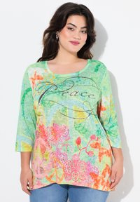 Farbiger, leichter Langarm-Top in Grün mit floralen Mustern, ausgestattet mit orangefarbenen und rosafarbenen Akzenten. "Frieden"-Text mit dekorativen Nähten.