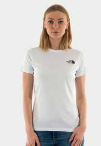 Valkoinen lyhythihainen T-paita, joka on valmistettu kevyestä puuvillasta, ja siinä on musta logo vasemmalla rinnassa sekä perinteinen pyöreä kaula-aukko.