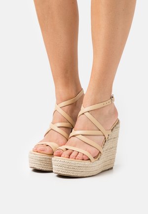 Beige strappy wedge sandaalit, joissa on kudottu juuttialustava. Hihnat risteävät jalan päällä ja niissä on säädettävä nilkkasolki.