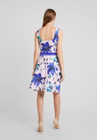 Floral dress in light pink with large blue and teal flowers. Sleeveless with a scoop back design and a fitted waist, flaring into a skirt.