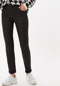 Pantalones negros ajustados, hechos de un material suave con un ligero brillo, con un diseño clásico de cinco bolsillos y puños enrollados, combinados con zapatillas blancas.