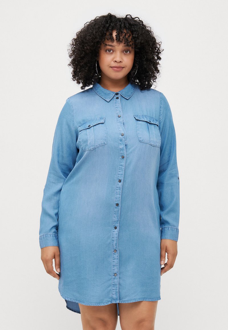 Heledad denimsärk kleit helesinises värvitoonis, nööpidega esitamine, terava kraega, kahe rinna taskuga, pikad varrukad ja veidi kõver äär.