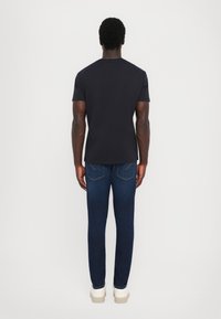 Svart kortermet t-skjorte kombinert med mørkeblå denimjeans, med slank passform og standard baklomme-design. Lyse sko.