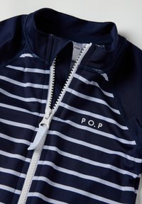 Laivastonsininen ja valkoinen raidallinen vetoketjullinen uimapuku, jossa on korkea kaulus ja P.O.P. logo. Suunniteltu sileästä, joustavasta materiaalista, jossa on etuvetoketju.