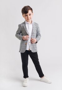 Marynarka w czarno-białą kratę, z detalem w postaci guzika, zestawiona z białą koszulą, czarnymi spodniami i białymi trampkami. Gładki, dopasowany krój.