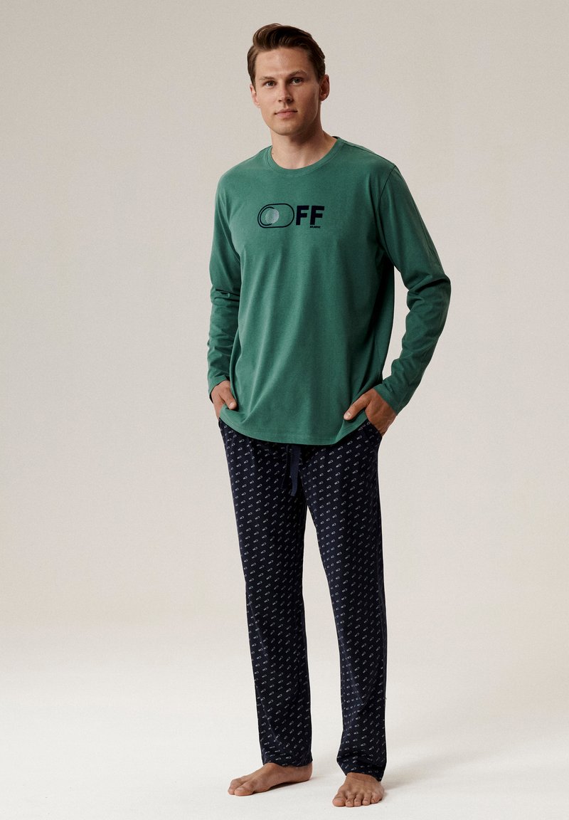 Zielona koszulka z długim rękawem z grafiką "OFF", zestawiona z granatowymi spodniami dresowymi z białymi akcentami wzoru i wiązanym pasem.