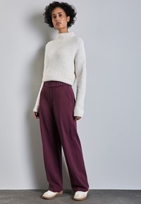 Maglione bianco soffice a maglia con polsini a coste, abbinato a pantaloni larghi bordò a vita alta e sneakers bianche con dettagli beige.
