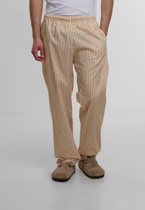 Tan and cream striped pajama pants with elastic waistband, smooth fabric texture, relaxed fit, worn with beige slip-on footwear.
