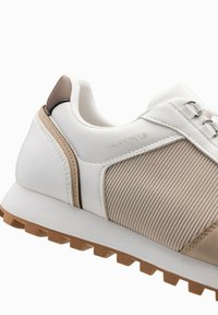 Baskets de sport blanches et beige avec une tige texturée, dotées de lacets, d'une semelle en caoutchouc et d'un discret logo. Design léger et structuré.