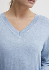 Helles blaues, gestricktes Sweatshirt mit V-Ausschnitt. Weiche Textur und gerippte Ränder am Ausschnitt und an den Ärmeln. Lässige Passform.