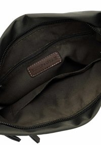 Nylon bag interior in dark green with zip pocket and brown leather label. Smooth texture with sleek edges and stitching detail.