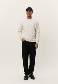Sweat-shirt crème avec un col rond et un détail logo, associé à un pantalon noir et des chaussures noires. Texture unie, coupe décontractée.