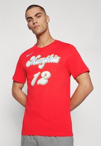 T-shirt en coton rouge avec un graphisme "Memphis" en blanc et bleu, avec "12" en dessous. Design à manches courtes et col rond.